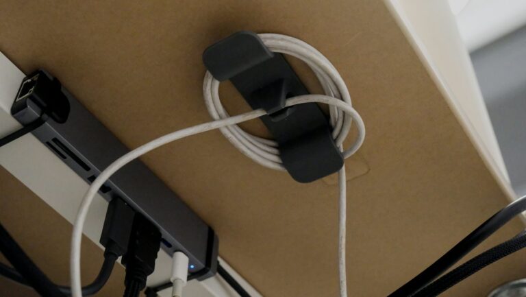 A cable organizer holding a coiled white cord under a desk