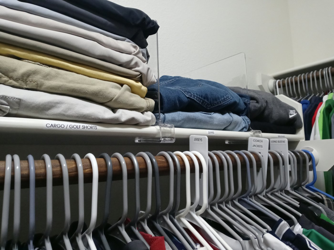 Folded clothing on a closet shelf separated by clear dividers